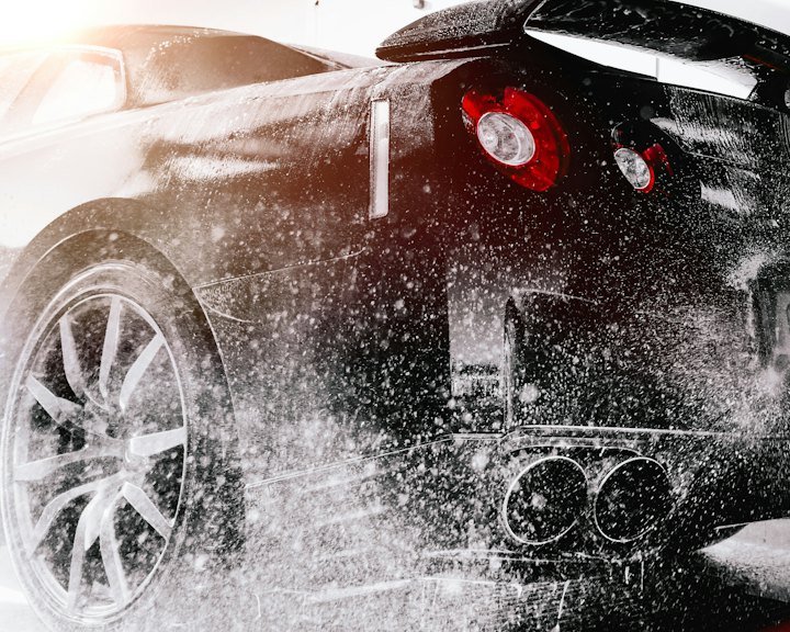 A car covered in snow foam being rinsed with a pressure washer