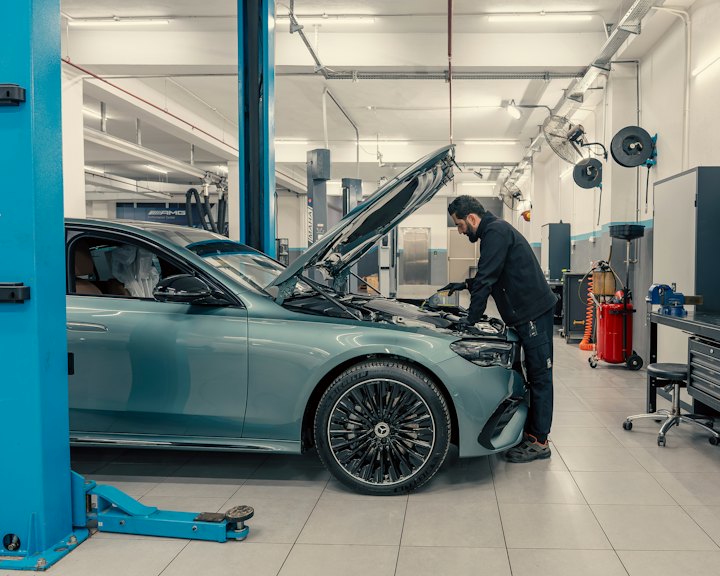 A mechanic working under the hood of a car in a bright, clean workshop